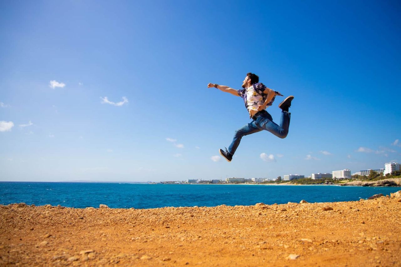 man in black shirt jumping on brown sand near body of water during daytime